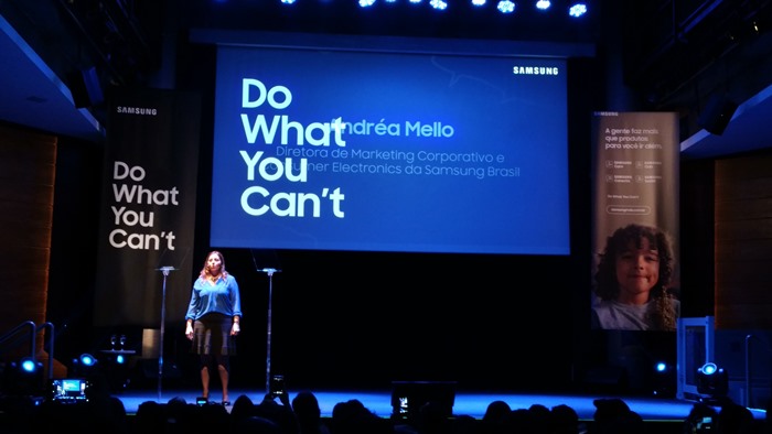 Imagem de Andréa Mello no palco. Na tela, está escrito o lema da campanha, em letras grandes, "Do What You Can't"